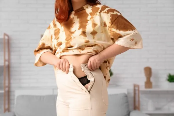 Image of woman trying to do her trousers up after pregnancy weight gain Stevenage Ware